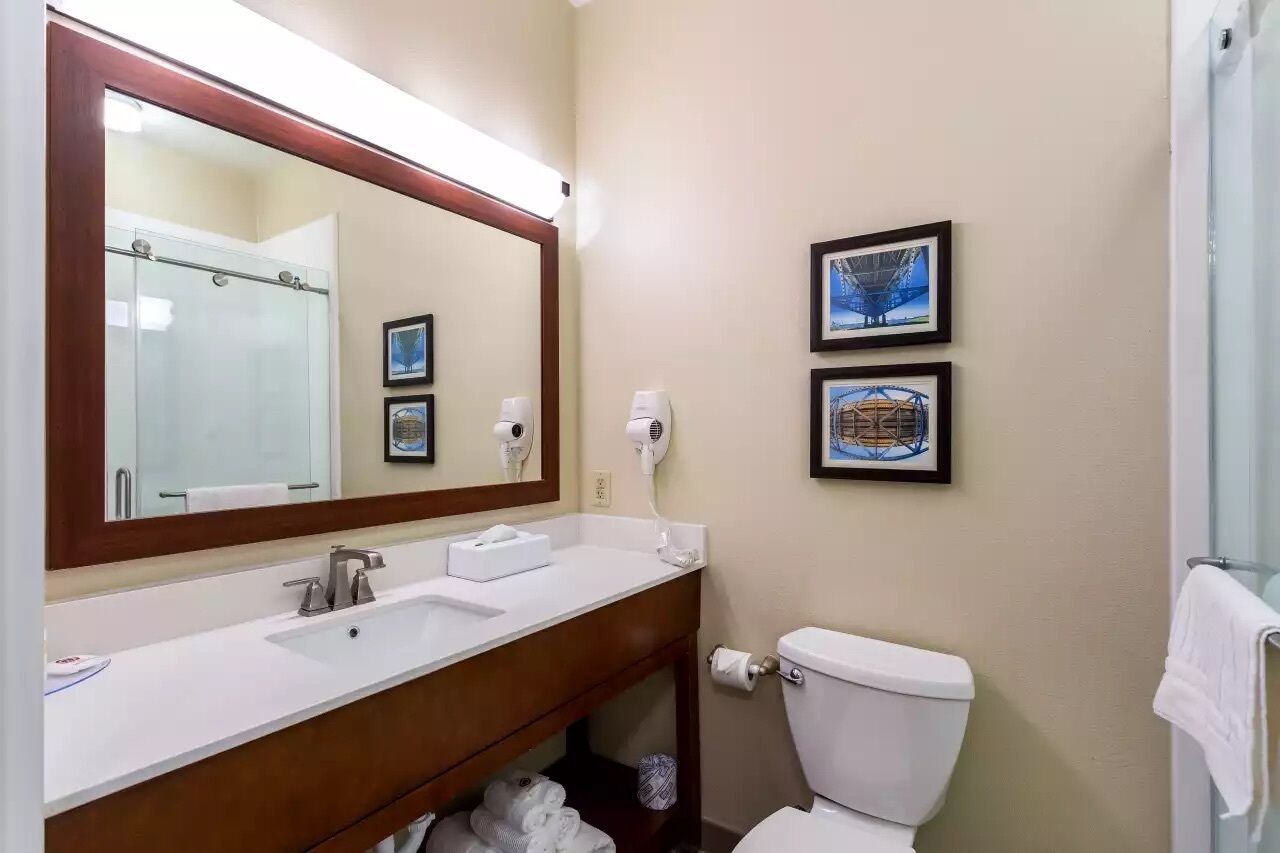 A bathroom with a white sink, a large mirror, a toilet, and two framed pictures on the wall.