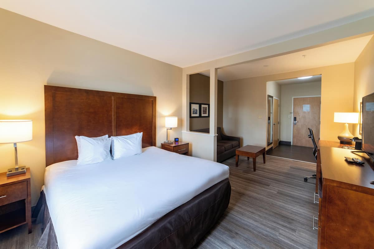 Una habitación de hotel con una cama grande, mesitas de noche con lámparas, un escritorio, una silla y un espejo.