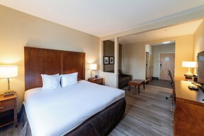 A hotel room with a large bed, bedside tables with lamps, a desk, a chair, and a mirror.