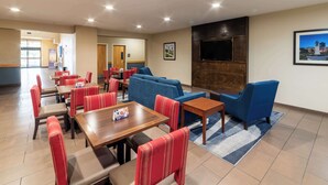 A hotel lobby with red and blue seating, a TV mounted on the wall, and a wooden table with a placemat. - Sonesta Essential - Baton Rouge Airport (Baton Rouge)