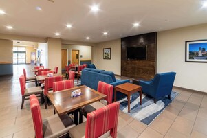 Un hall de hotel con asientos rojos y azules, un televisor montado en la pared y una mesa de madera con posavasos.