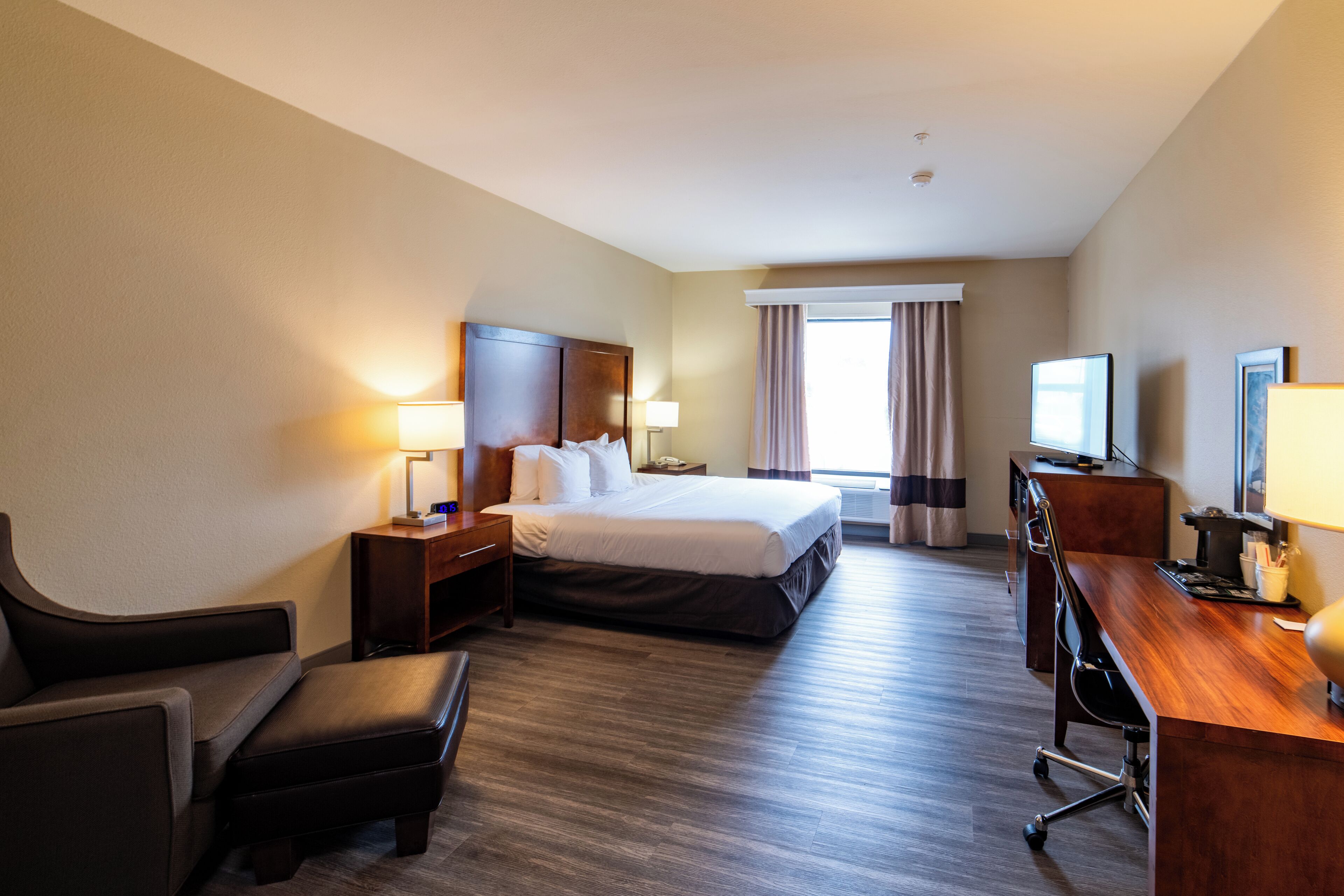 A hotel room with a bed, a desk, a chair, a TV, and a window with curtains.