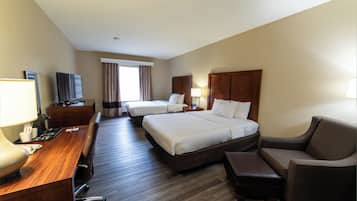 A hotel room with two beds, a desk with a computer, a TV, and a window with curtains.