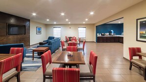 A spacious lounge area with multiple seating options including sofas and tables, a kitchen area in the background, and a TV mounted on the wall. - Sonesta Essential - Baton Rouge Airport (Baton Rouge)