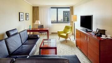 Una habitación de hotel con sofá, una mesita, televisor, lámpara y una silla.