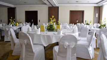 A banquet hall with round tables, white chairs, and floral centerpieces.