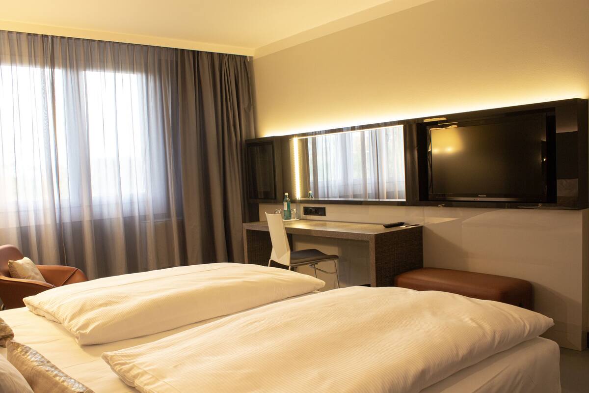 A hotel room with two beds, a desk, a chair, a television, and a window with curtains.