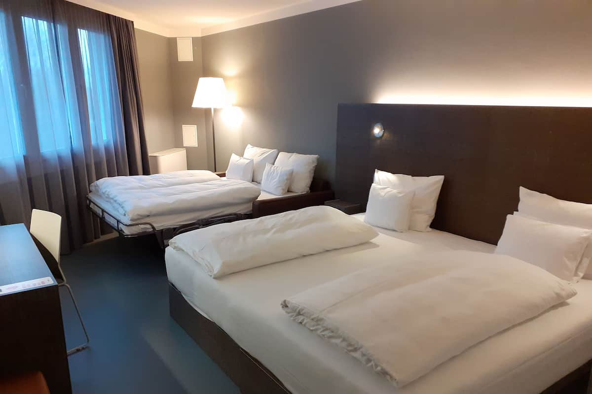 A hotel room with two beds, a desk, a chair, and a lamp.