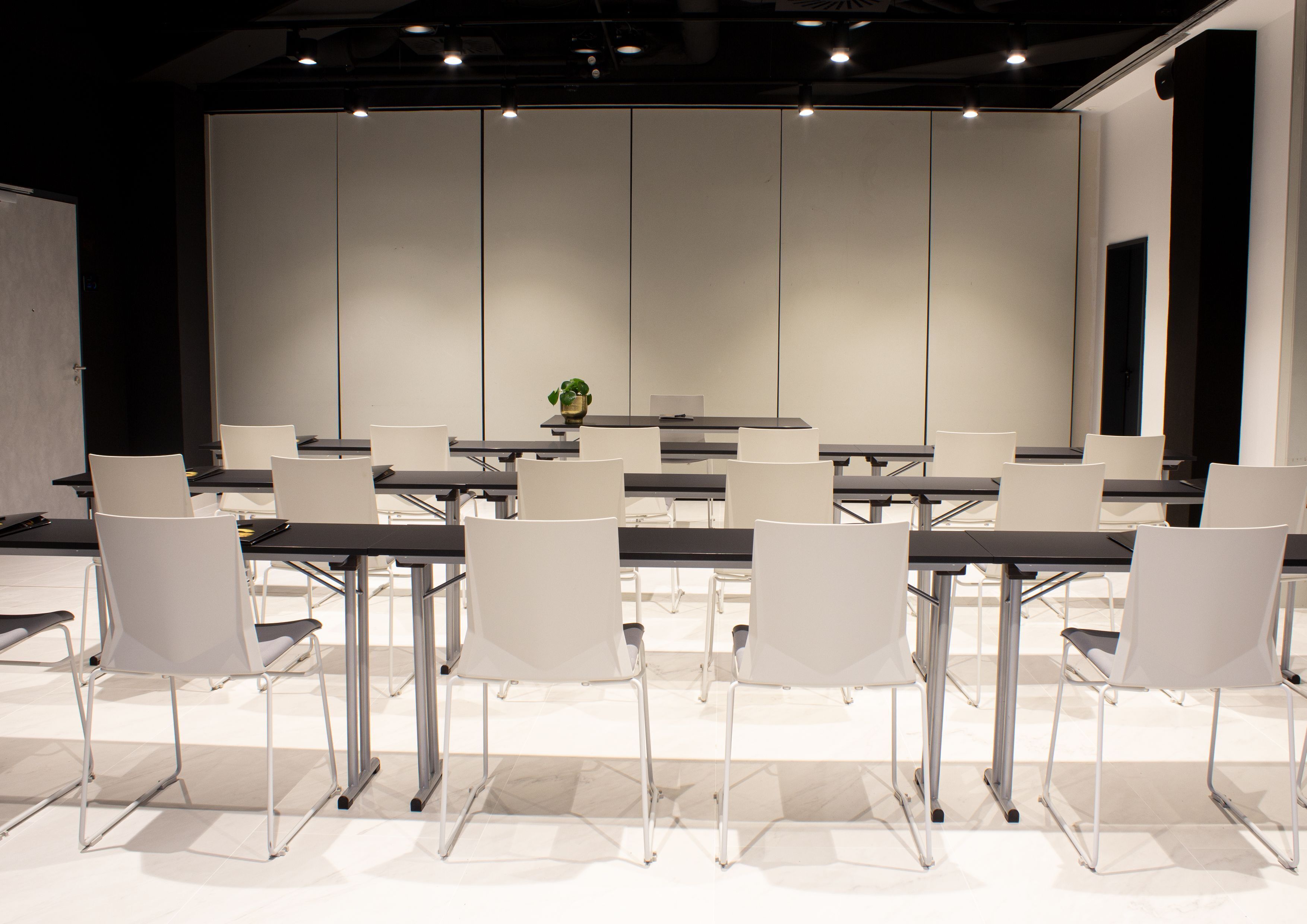 A conference room with a long table and white chairs, a plant on the table, and a whiteboard on the wall.