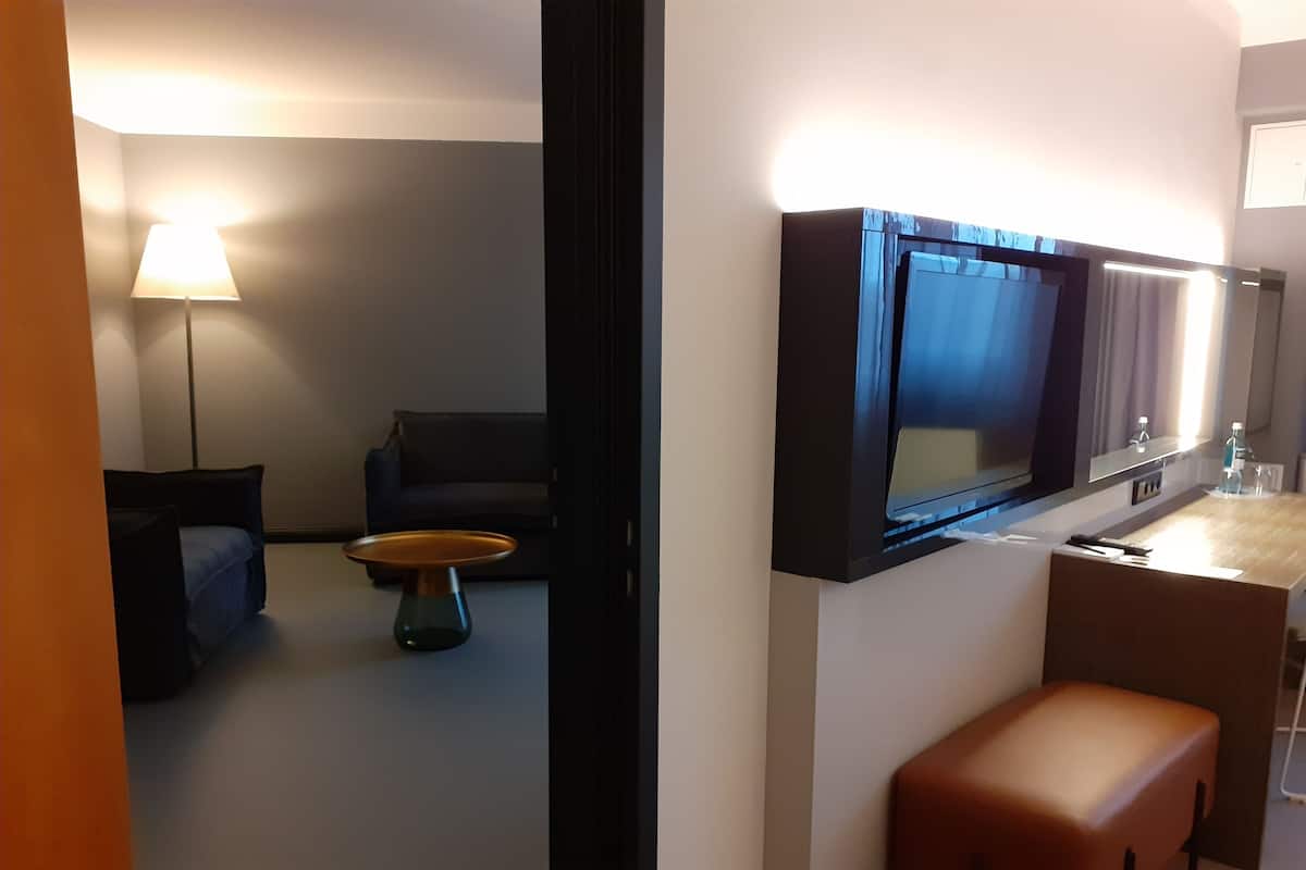 A modern hotel room with a flat-screen TV mounted on the wall, a sofa, a coffee table, and a bench.