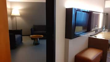A modern hotel room with a flat-screen TV mounted on the wall, a sofa, a coffee table, and a bench.