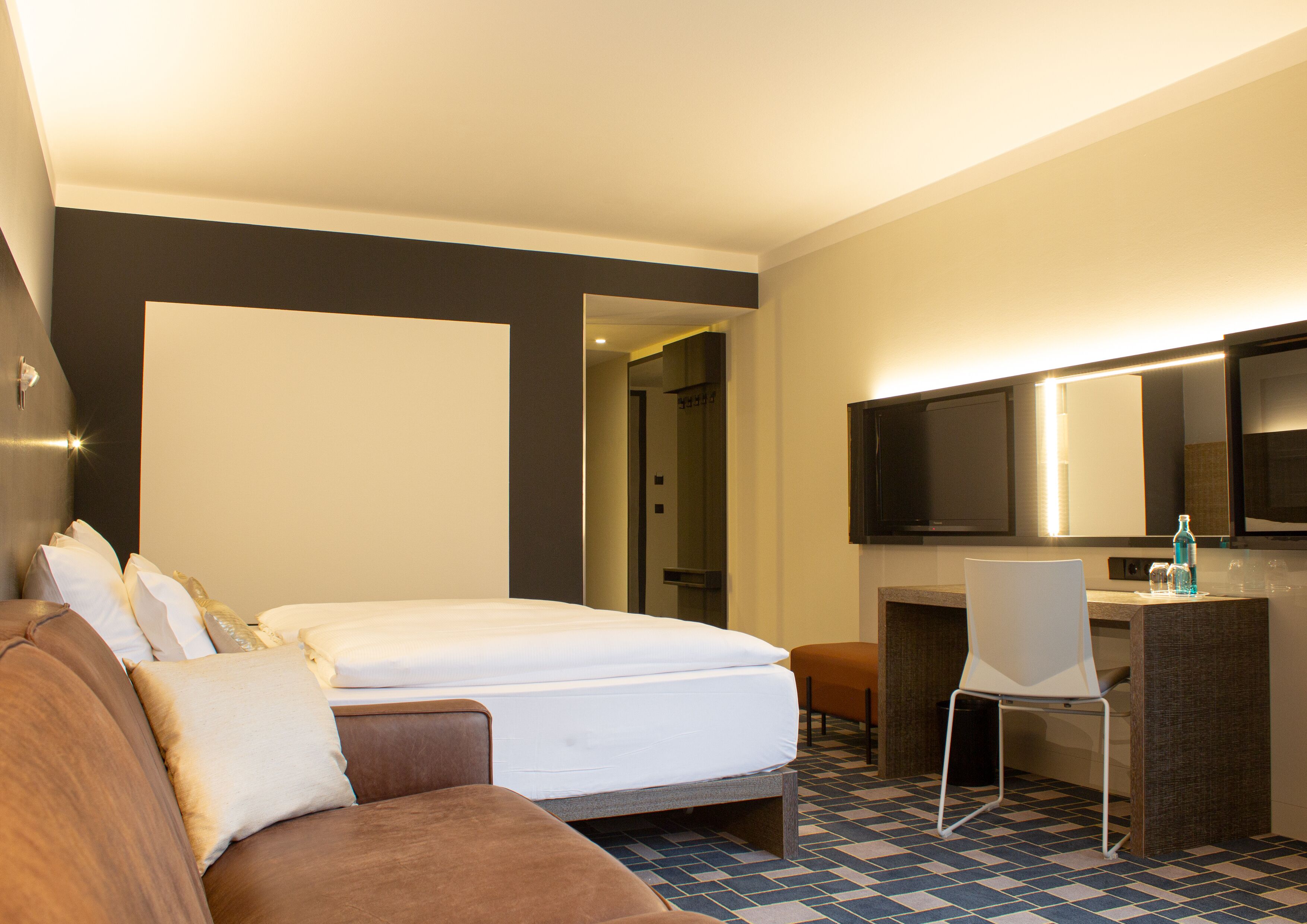 A hotel room with a bed, a sofa, a desk, and a television.