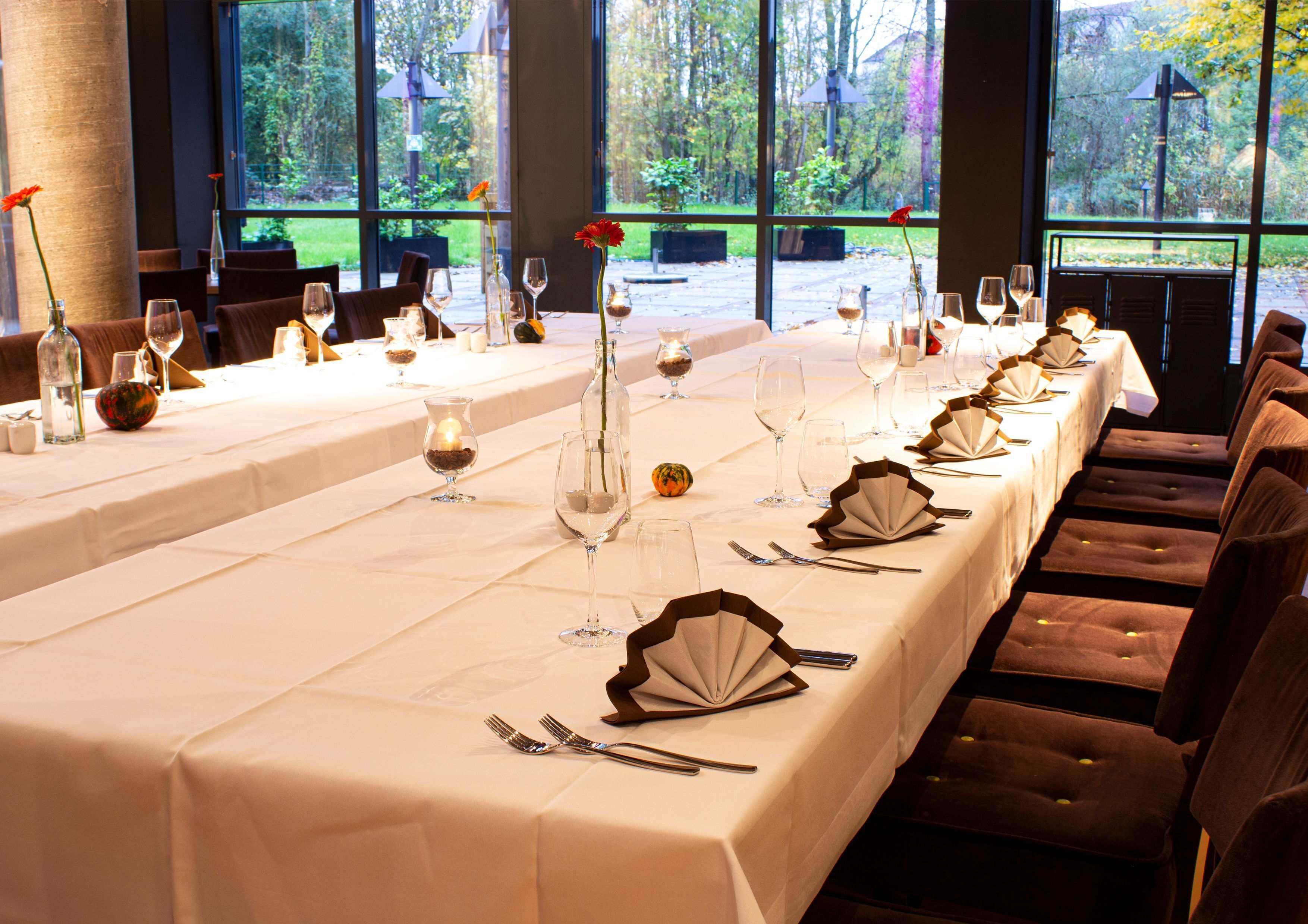 A long dining table set for a formal meal with multiple wine glasses, folded napkins, and a vase with a flower.