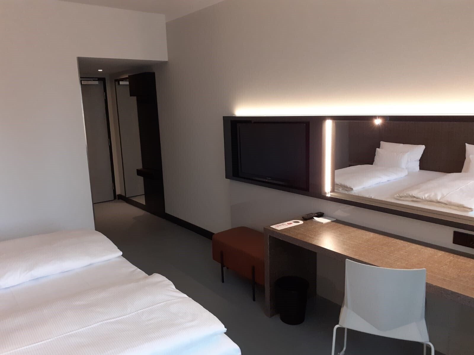 Une chambre d’hôtel avec deux lits, un bureau, une chaise, une télévision et une poubelle.