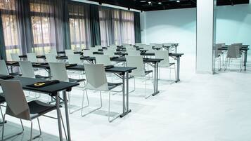 Ein Konferenzraum mit Tischen und Stühlen, großen Fenstern mit Vorhängen und einem gefliesten Boden.