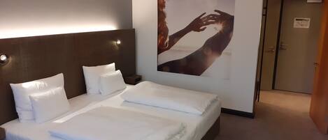 A neatly made bed with white linens, a dark headboard, and a wall-mounted artwork depicting a human figure.