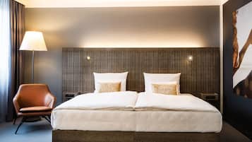 Una habitación de hotel moderna con una cama grande, una silla, una lámpara y un aplique de pared.