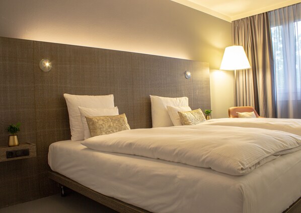 Une chambre d’hôtel avec un grand lit, deux tables de chevet, une lampe et une vue sur l’extérieur à travers les rideaux.