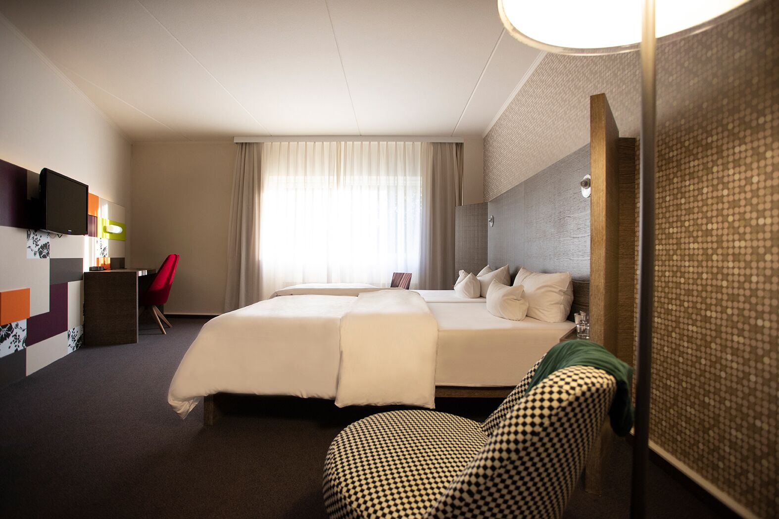 A hotel room with a large bed, a desk with a chair, a TV, and a window with curtains.
