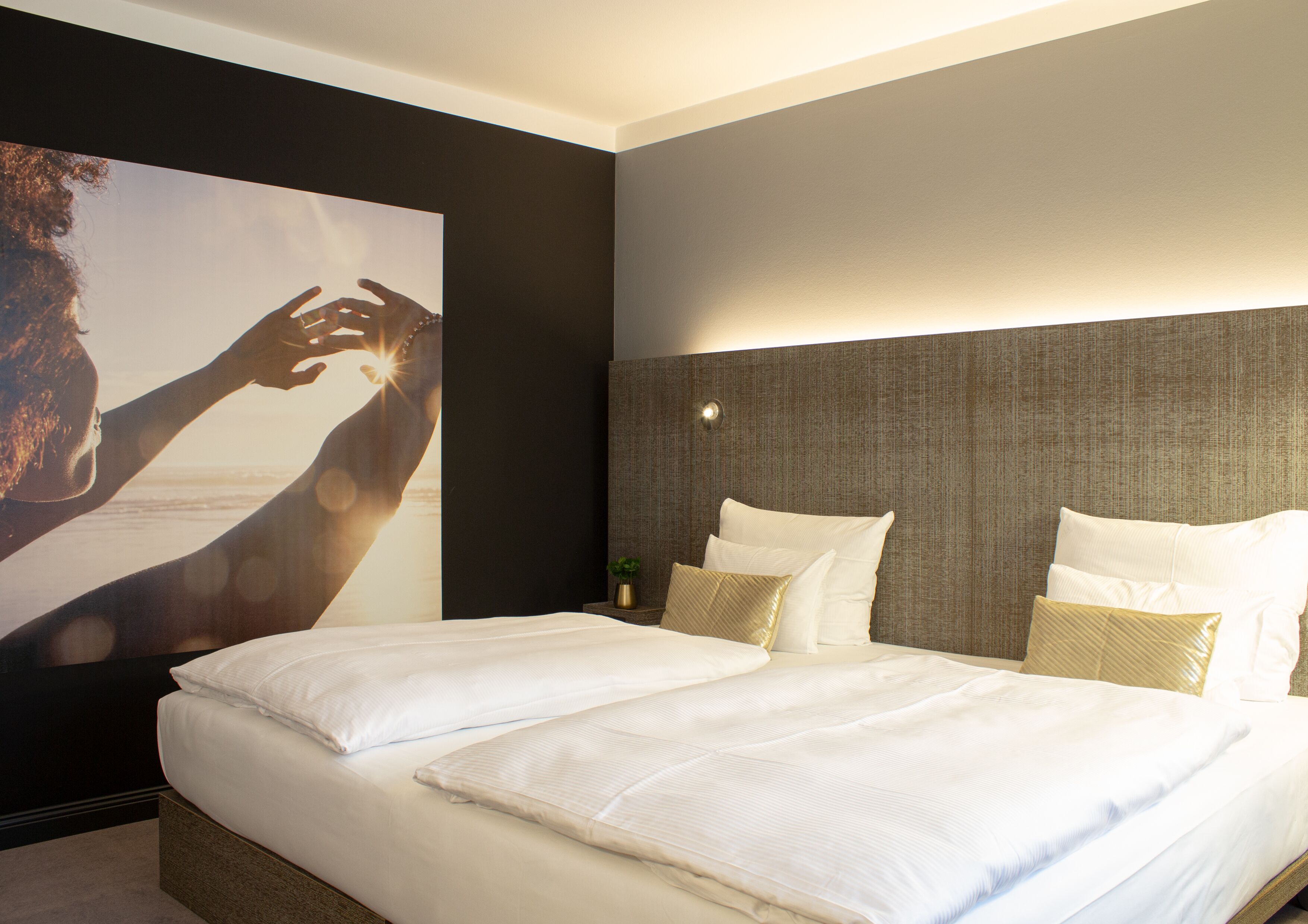 A modern hotel room with a large bed, a headboard with a textured design, and a wall-mounted light fixture.