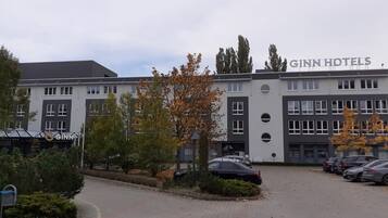 Ein GINN Hotels Gebäude mit Parkplatz und begrüntem Bereich mit Bäumen und Sträuchern.
