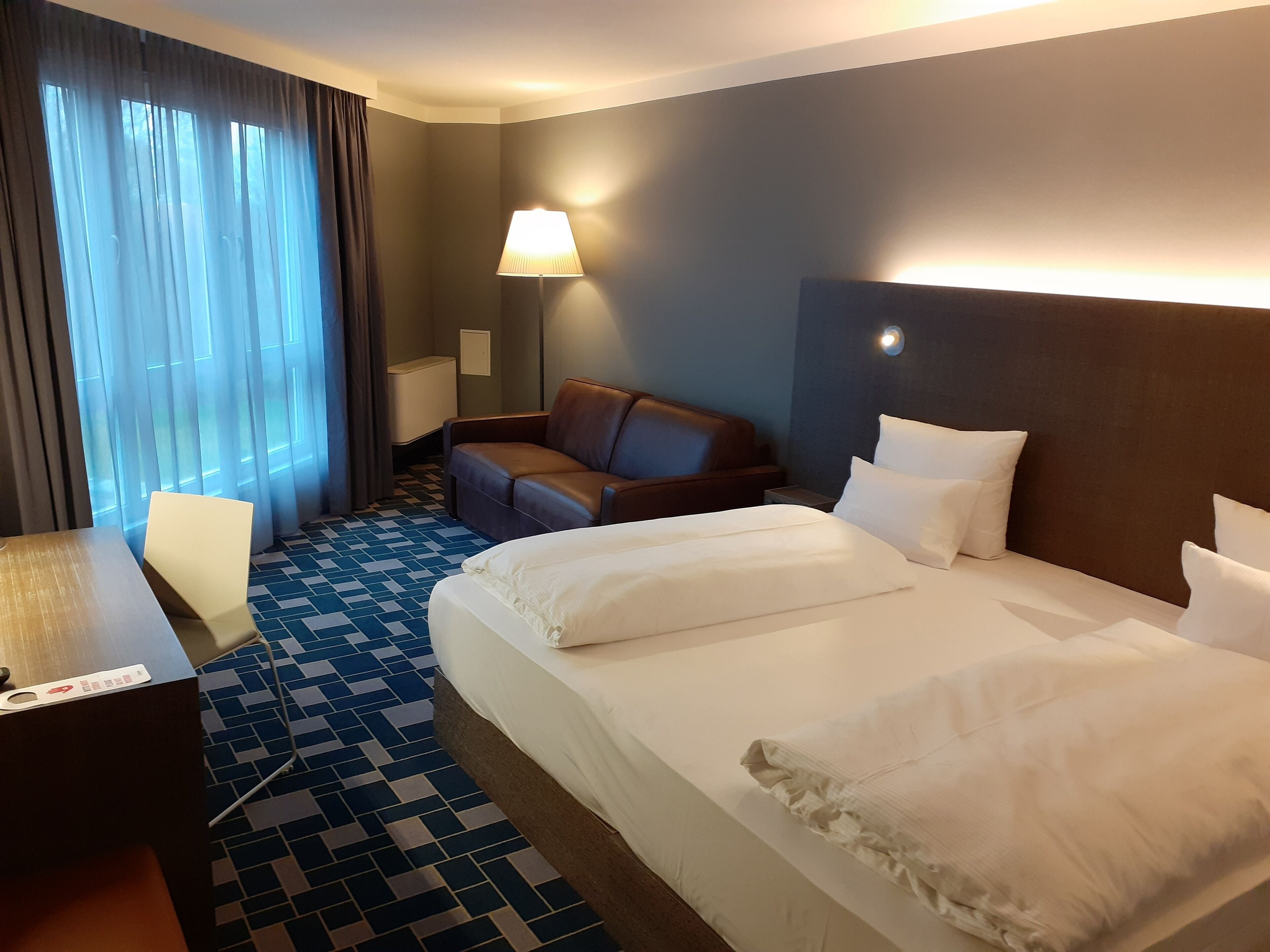 Una habitación de hotel con una cama grande, un escritorio, una silla, un sofá y una lámpara.