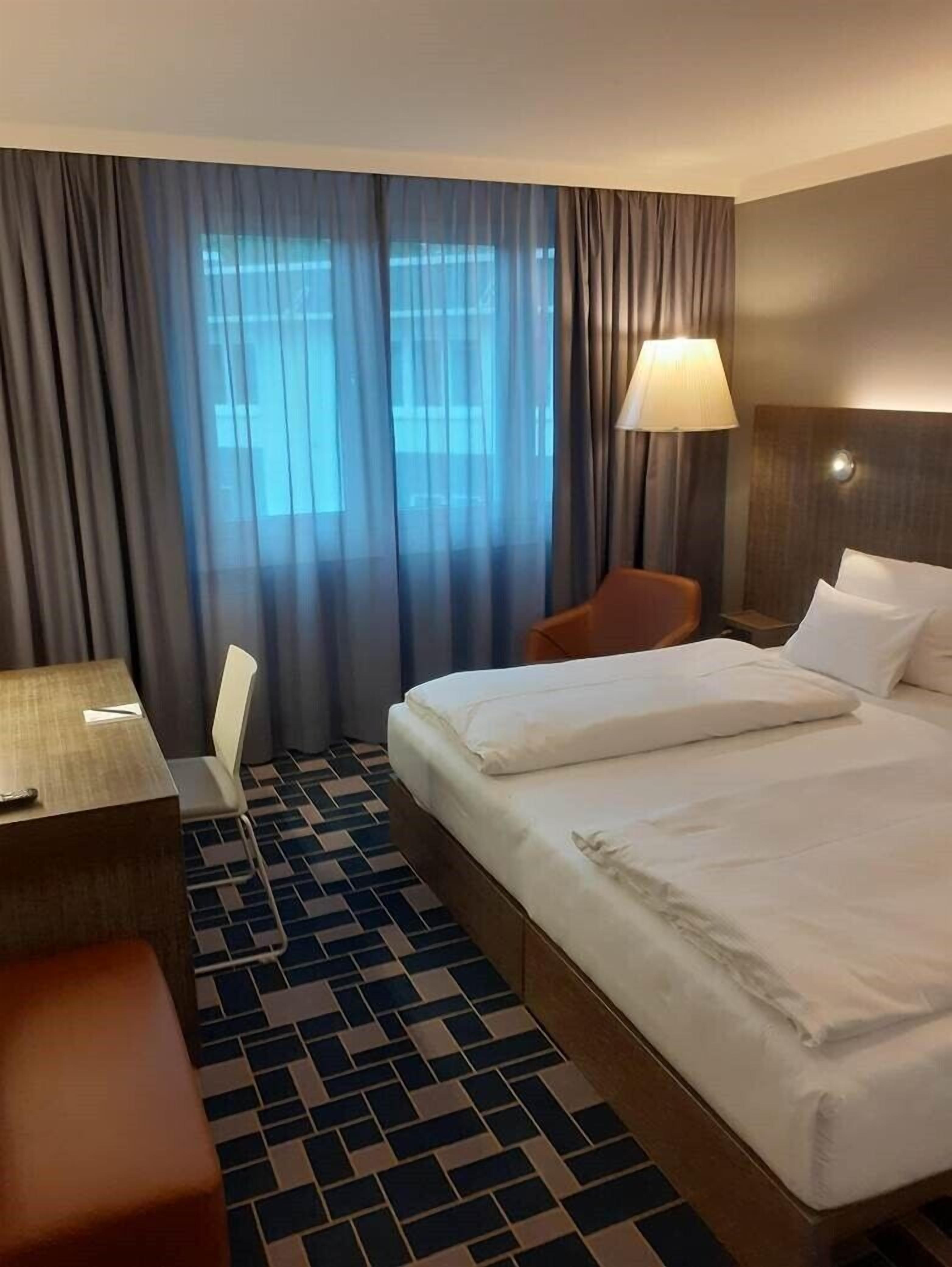 Una habitación de hotel con cama, escritorio, silla y lámpara.