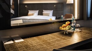 Una habitación de hotel con una cama, un escritorio con frutero, y un espejo que refleja la habitación.