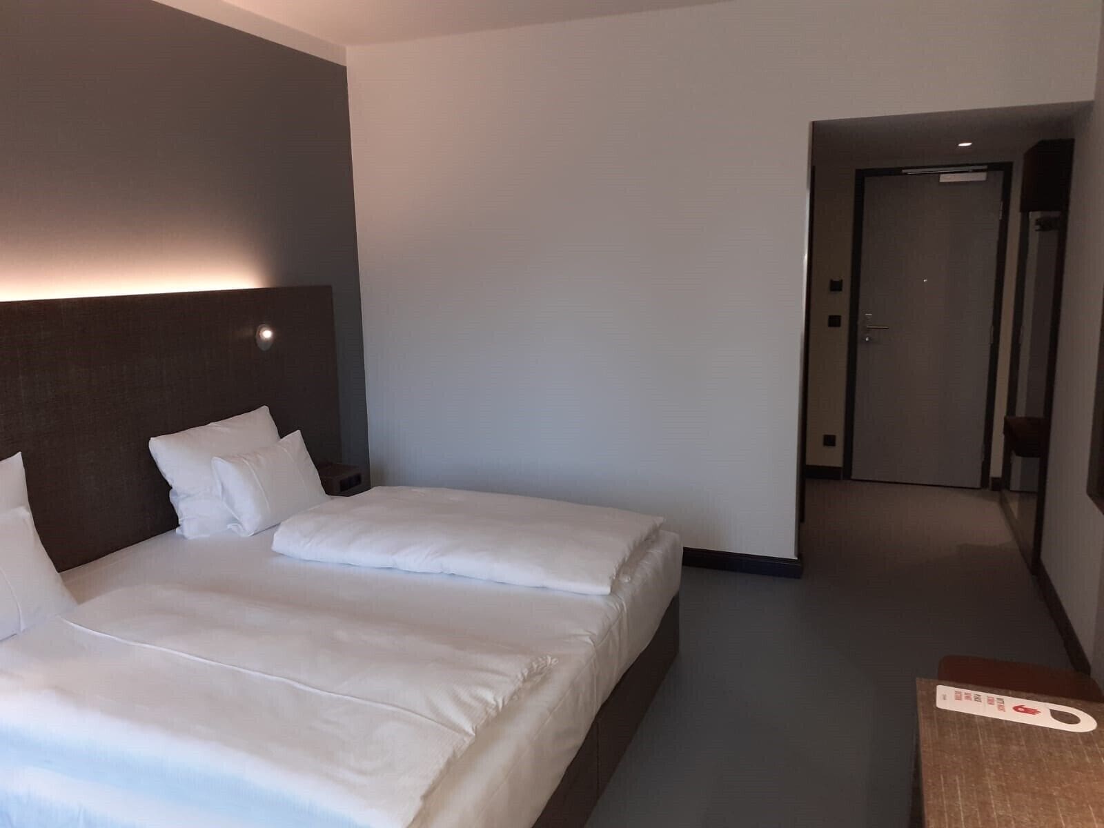 Une chambre d’hôtel avec un grand lit, une tête de lit, une table de chevet et une porte donnant sur une autre pièce.