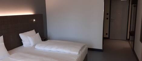 A hotel room with a large bed, a headboard, a bedside table, and a door leading to another room.