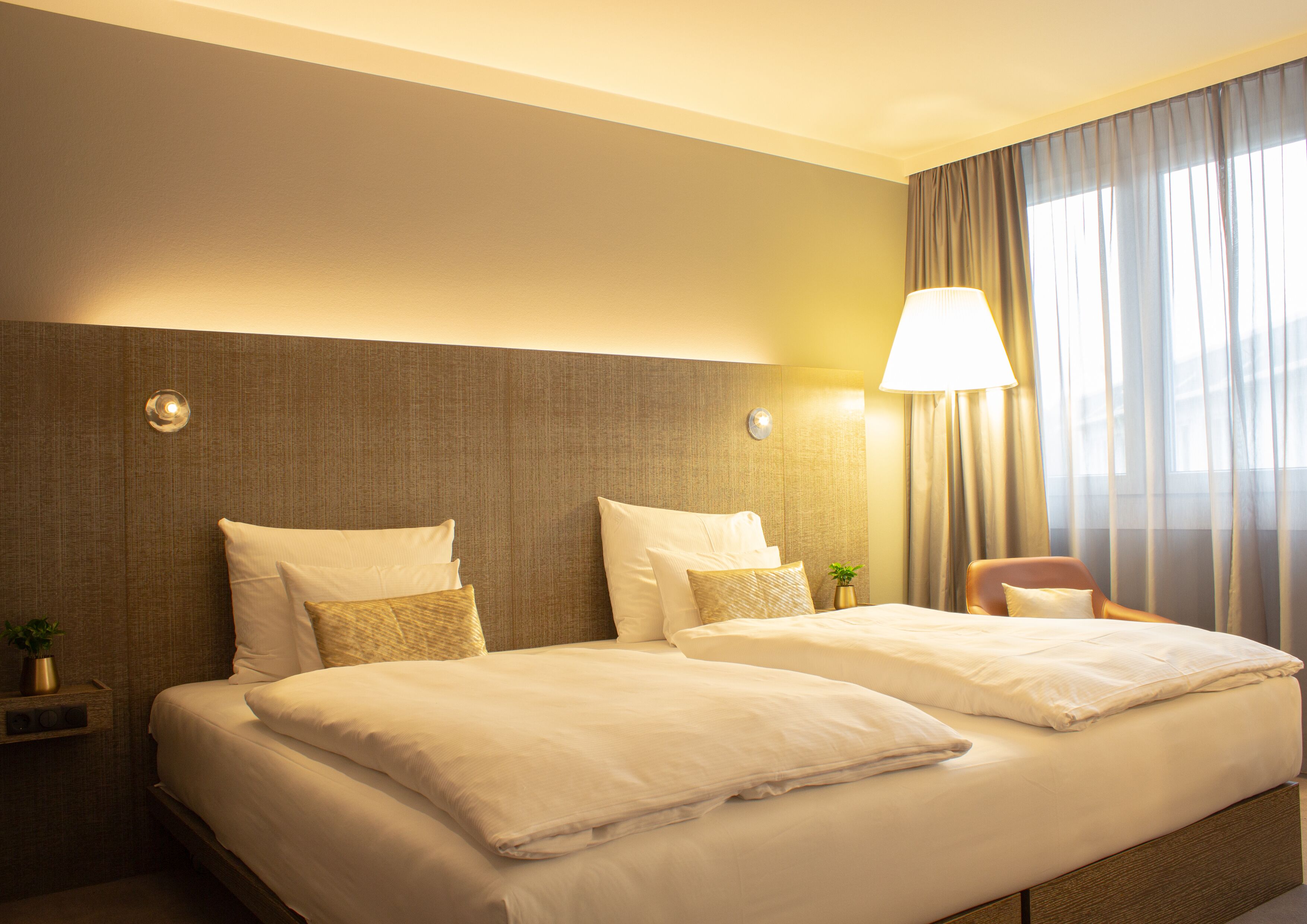 A hotel room with two beds, a nightstand, a lamp, and a chair.