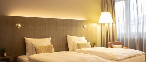 A hotel room with two beds, a nightstand, a lamp, and a chair.