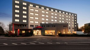 Ein modernes Hotel mit einer symmetrischen Fassade, zahlreichen Fenstern und einem markanten Eingang mit rotem Markisenvorzelt.
