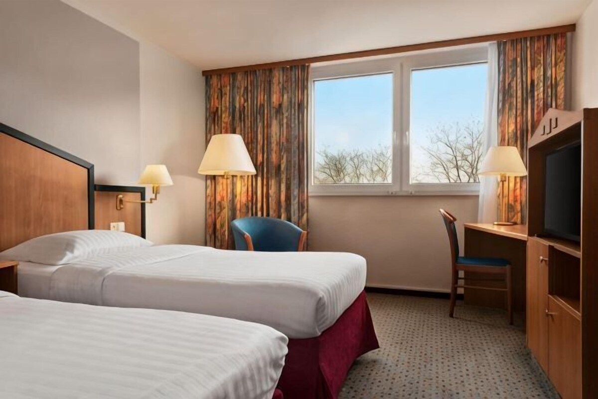 A hotel room with two beds, a desk, a chair, a TV, and a window with curtains.