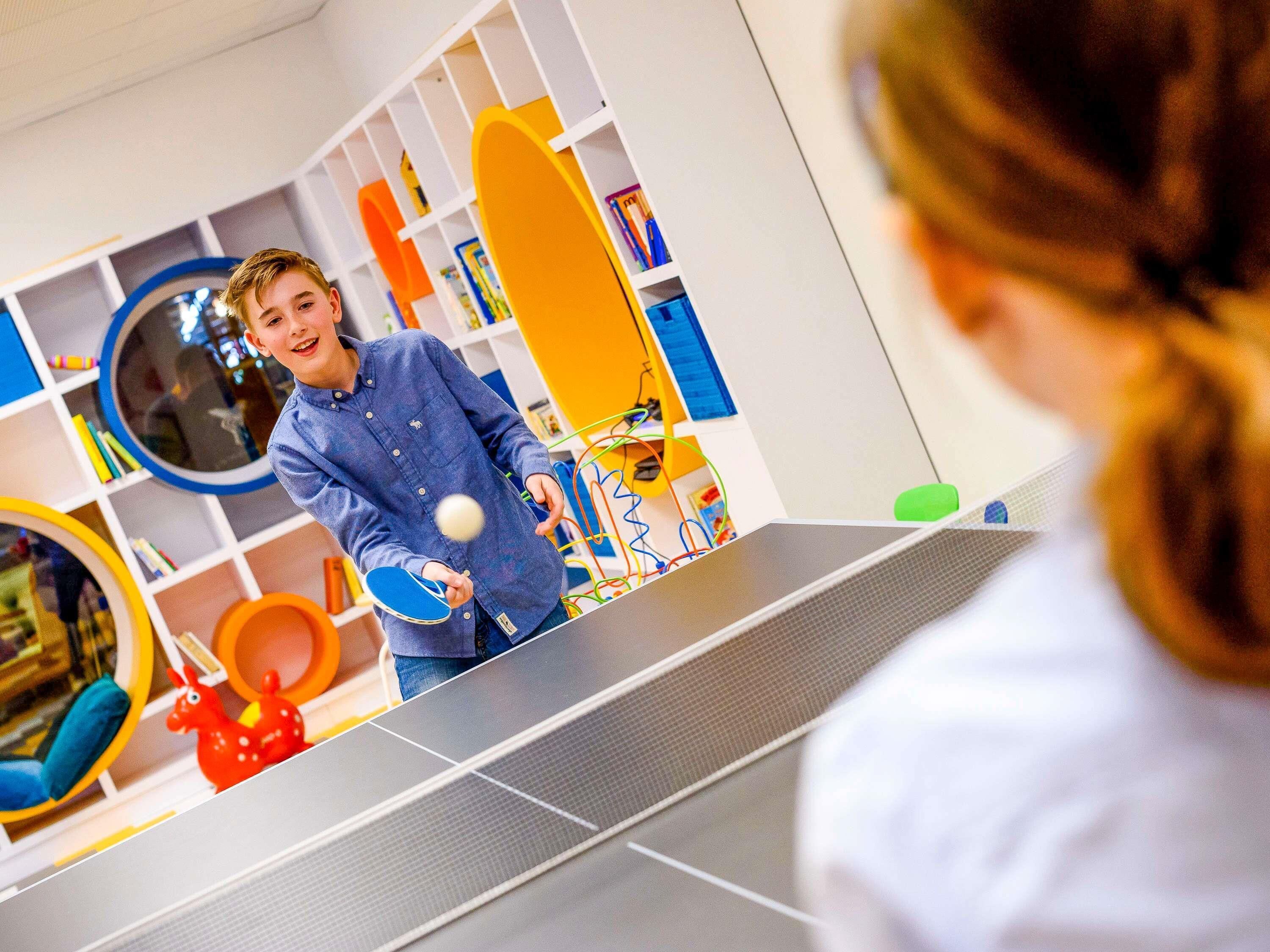 A ping pong table in a room with white walls and shelves containing books and toys.