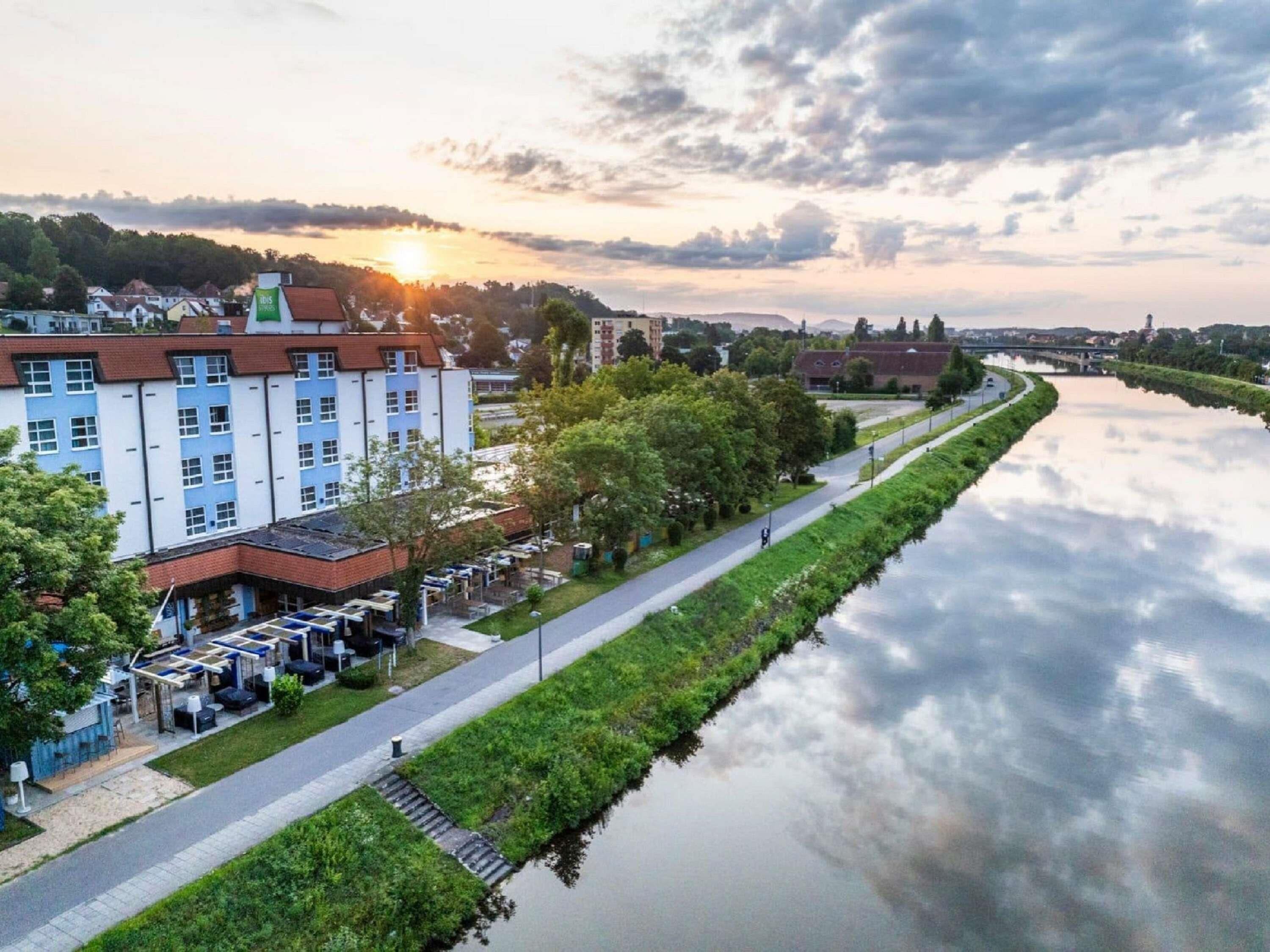 Ein Hotel am Flussufer mit einem langen Gebäude, einem gepflasterten Weg und einem ruhigen Fluss.