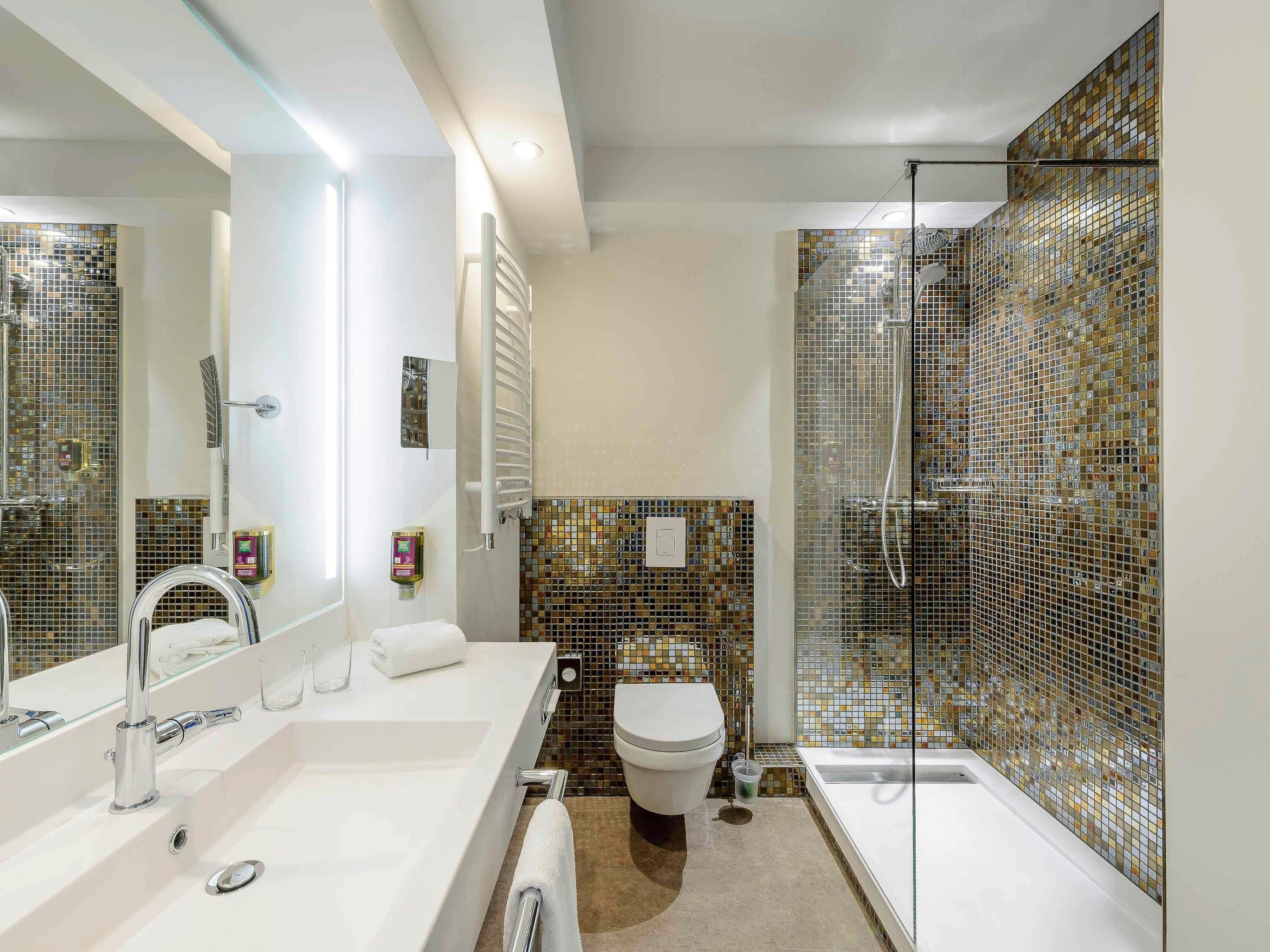 Un baño moderno con un espejo grande, un lavabo blanco, un inodoro y una zona de ducha.