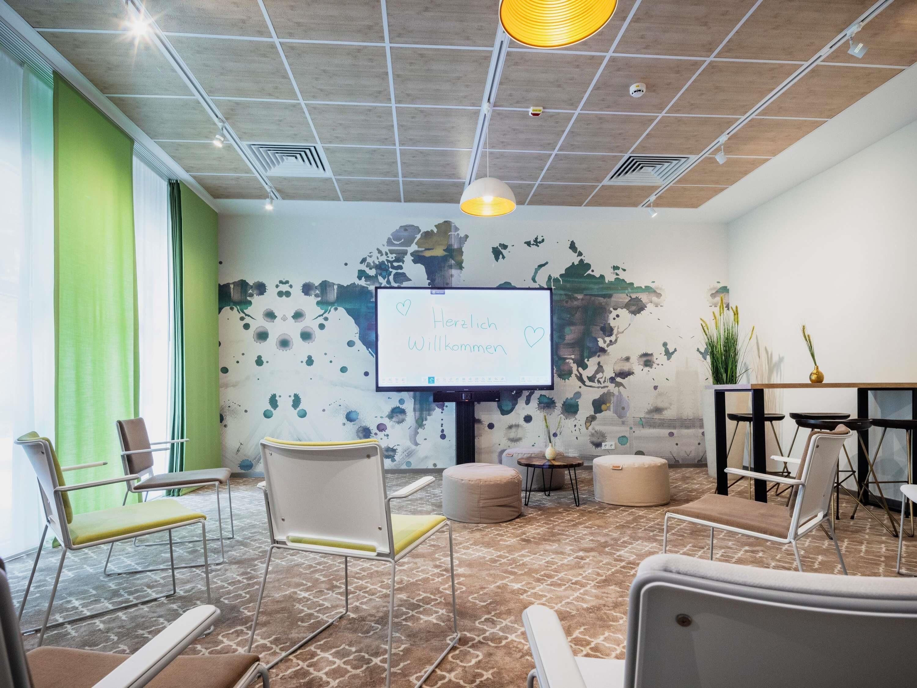 A conference room with a whiteboard, chairs, ottomans, a table, and a plant.