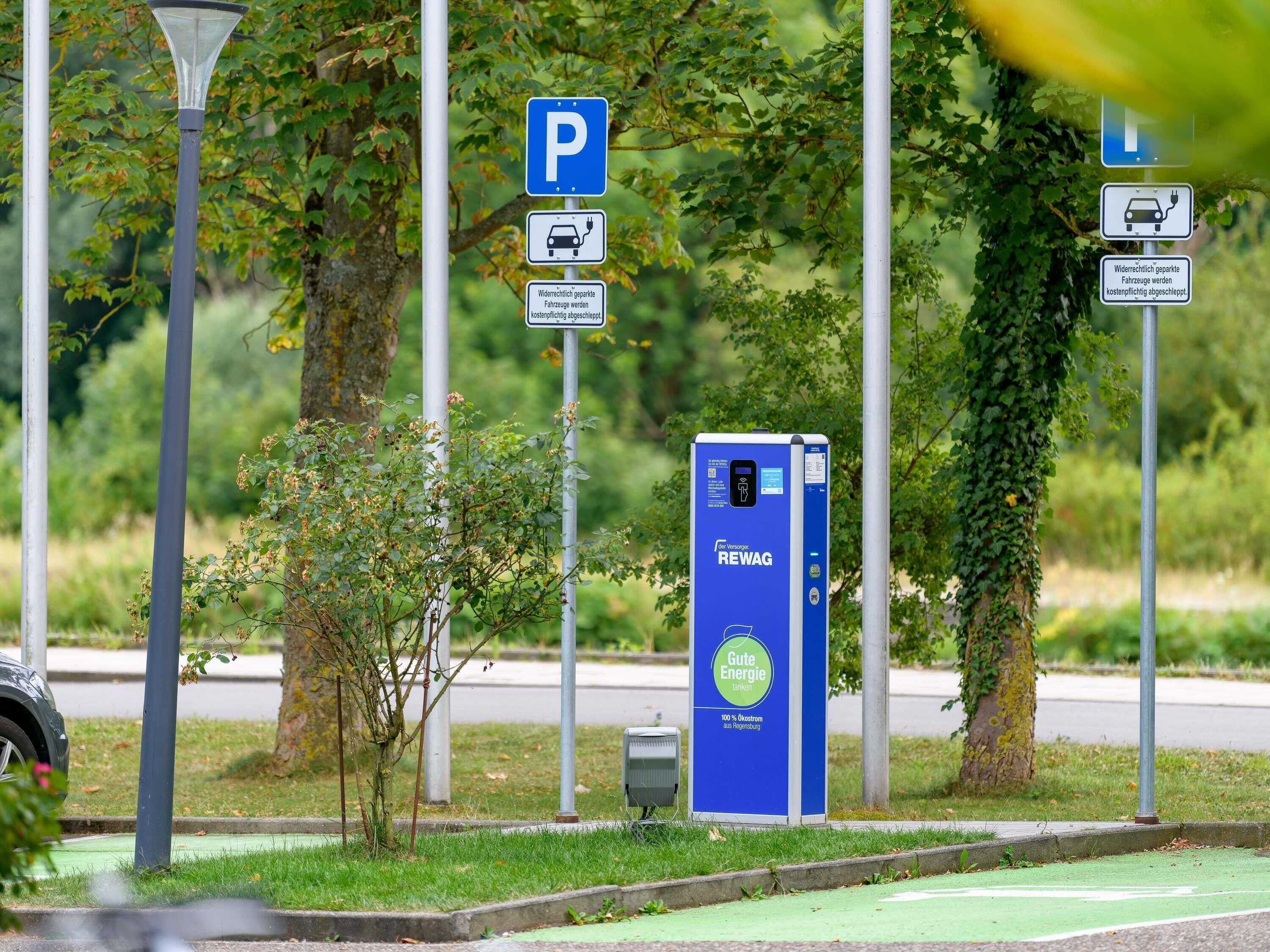 A parking area with electric vehicle charging stations, a blue information board, and a green bike lane.