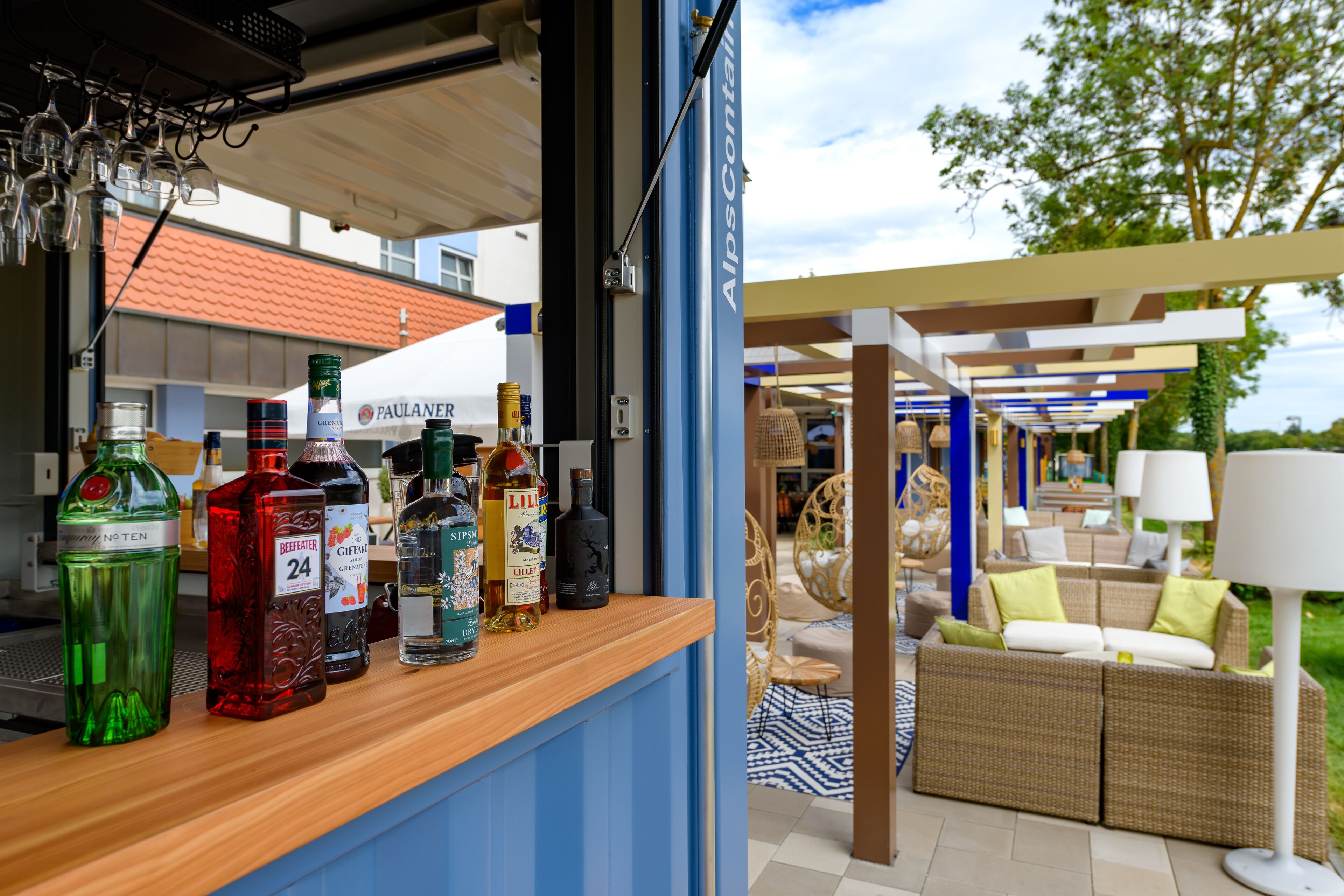 Zona de bar con diferentes botellas de licor, mobiliario de mimbre y vistas al exterior.