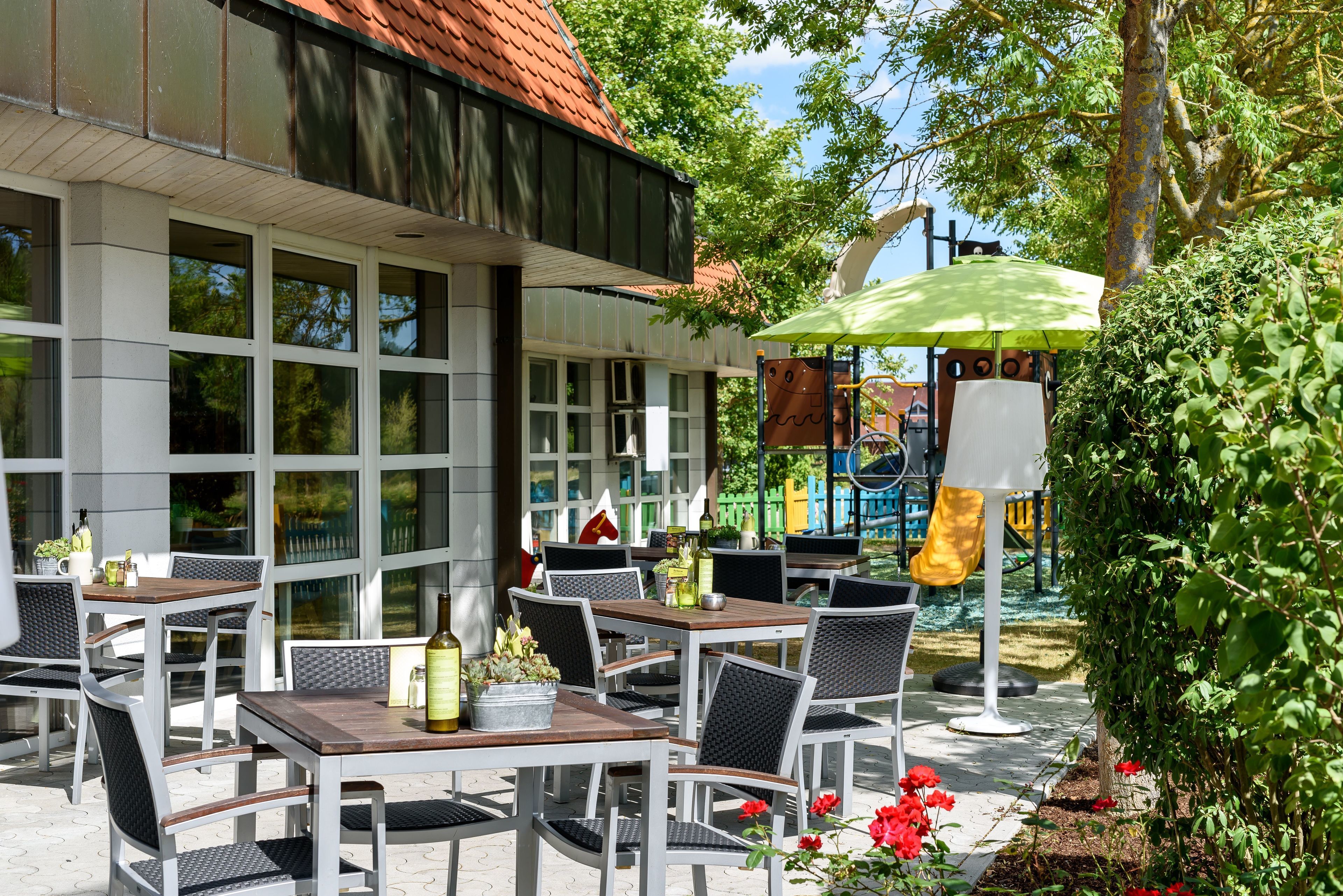 An outdoor seating area with tables and chairs, a play structure, and a garden with flowers.