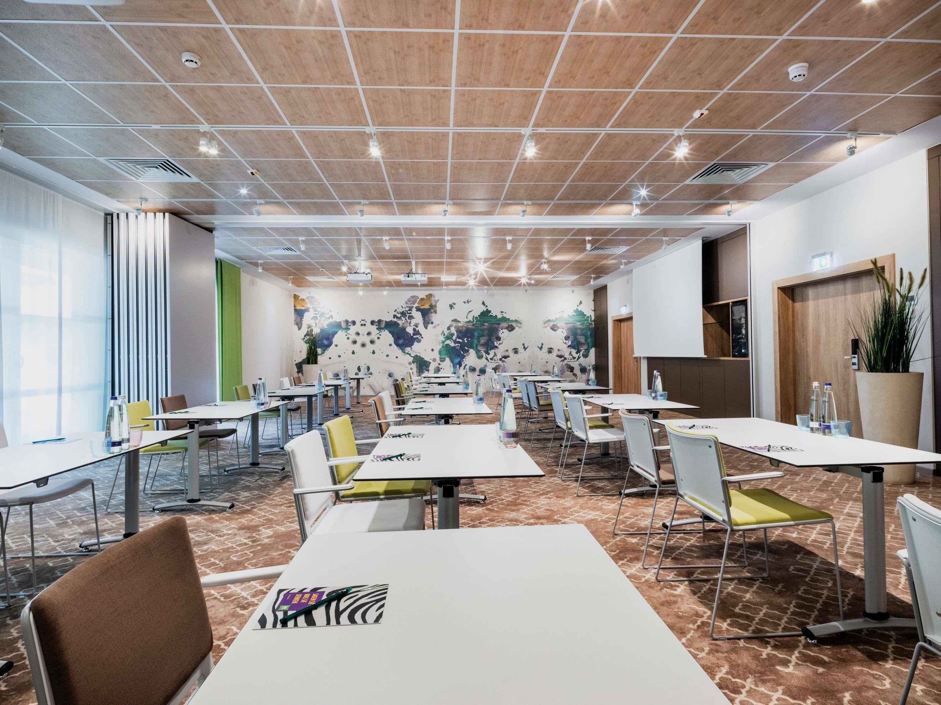 A conference room with tables, chairs, a world map mural, and a projector screen.