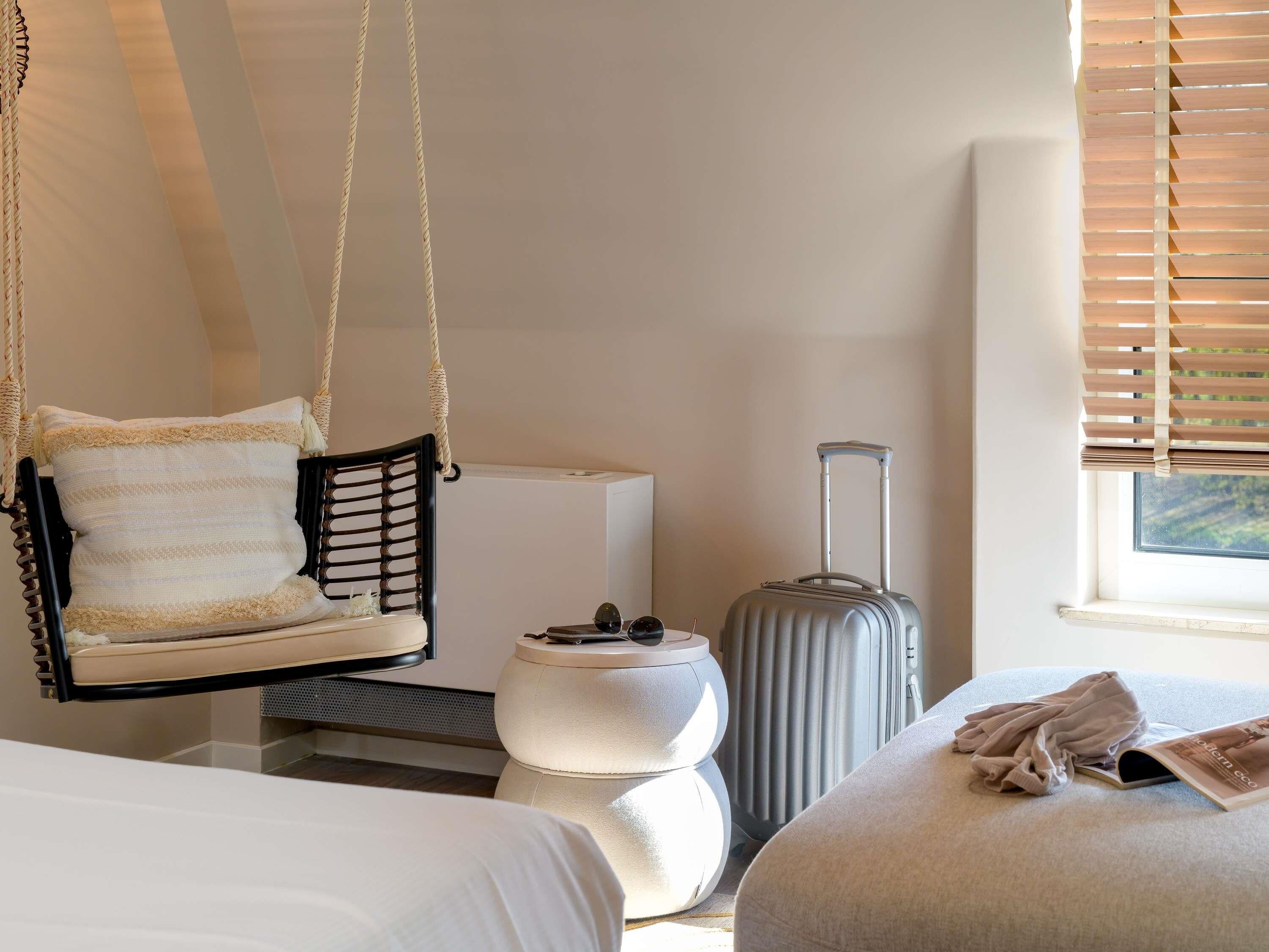 A room with a hanging chair, a suitcase, a bedside table, and a bed.