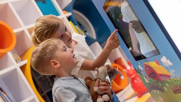 A child interacting with a digital display in a brightly colored room with shelves and toys.
