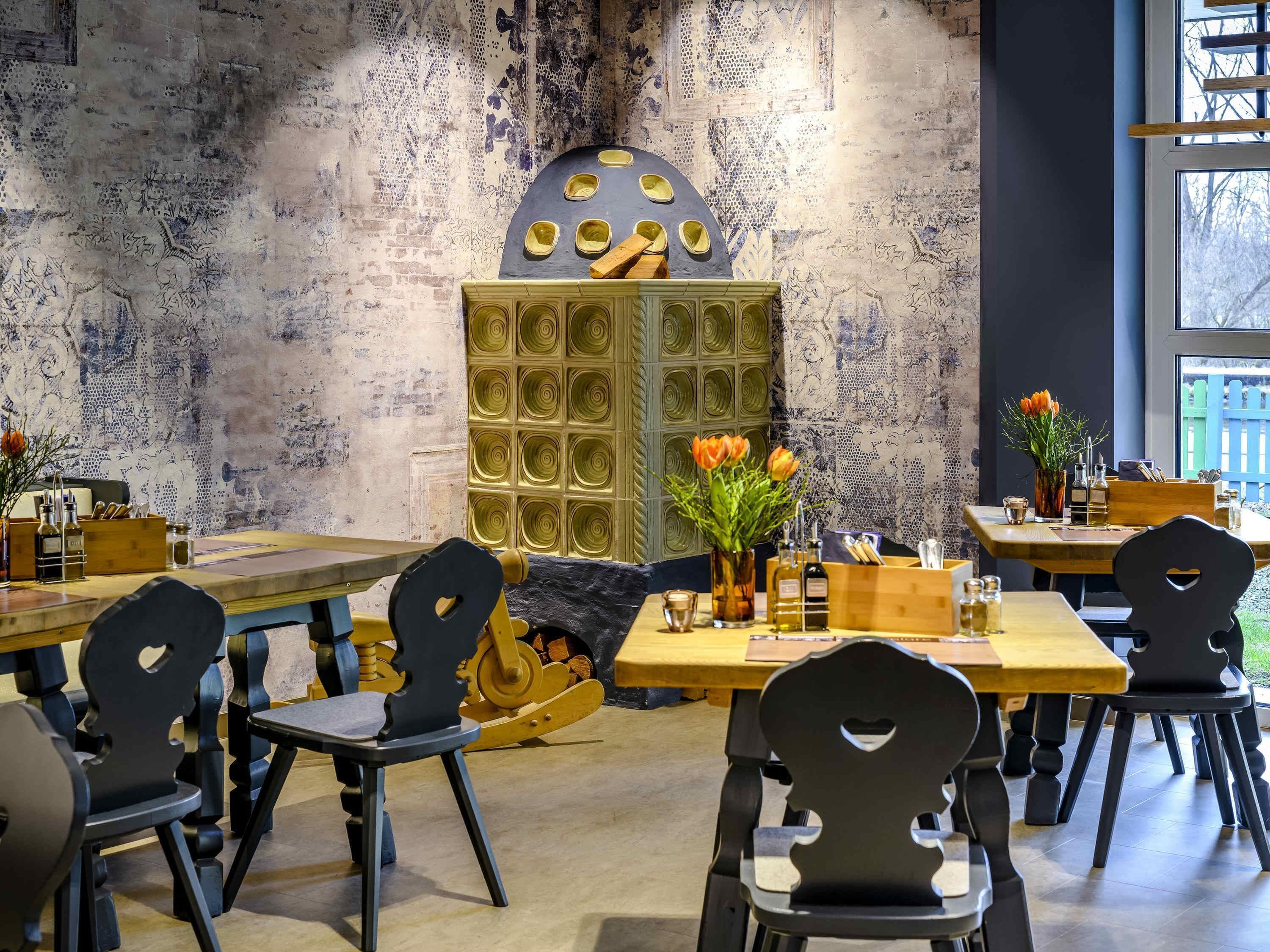 A restaurant interior with wooden tables and chairs, a central decorative element, and a view through a window.