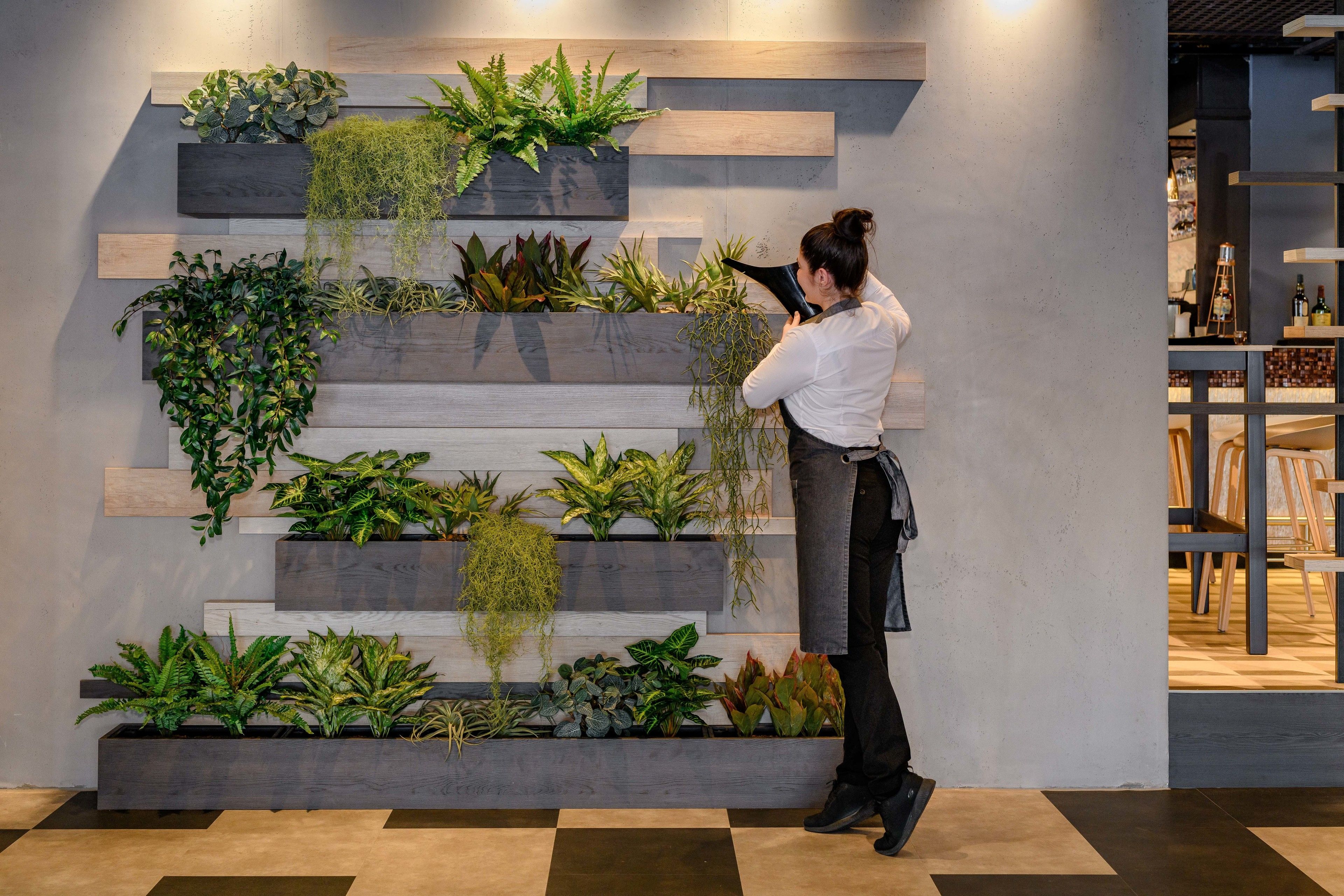 A modern interior with a vertical garden wall, wooden steps, and a person using a device.