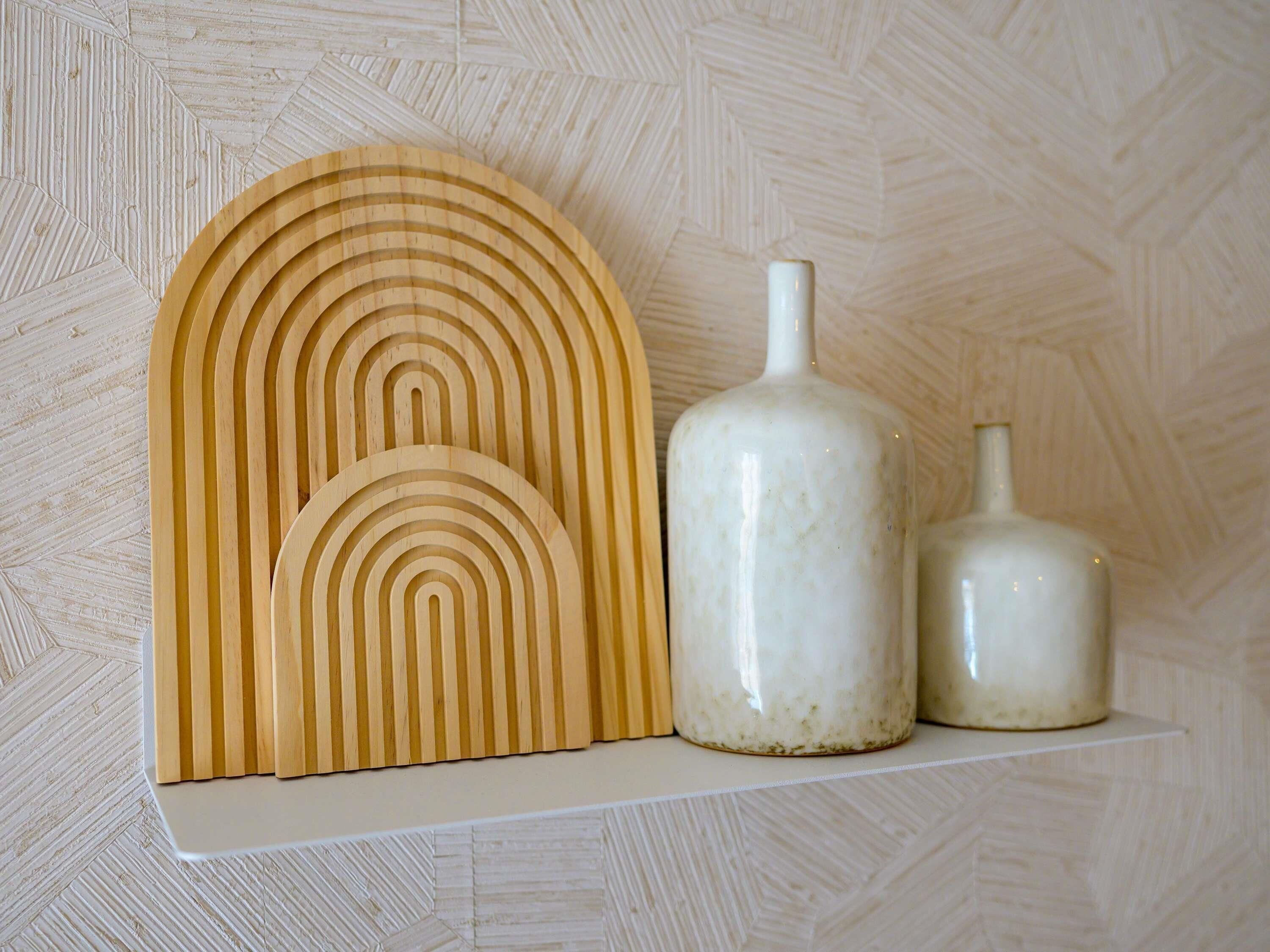 Una estantería con una obra de arte geométrico de madera y dos jarrones de cerámica blanca.