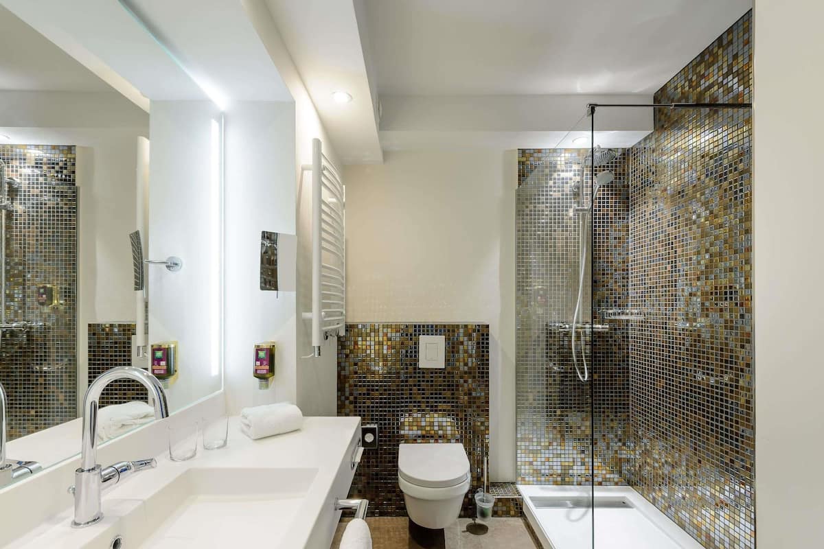Une salle de bain avec un lavabo blanc, des toilettes, une douche avec une porte en verre et un miroir.