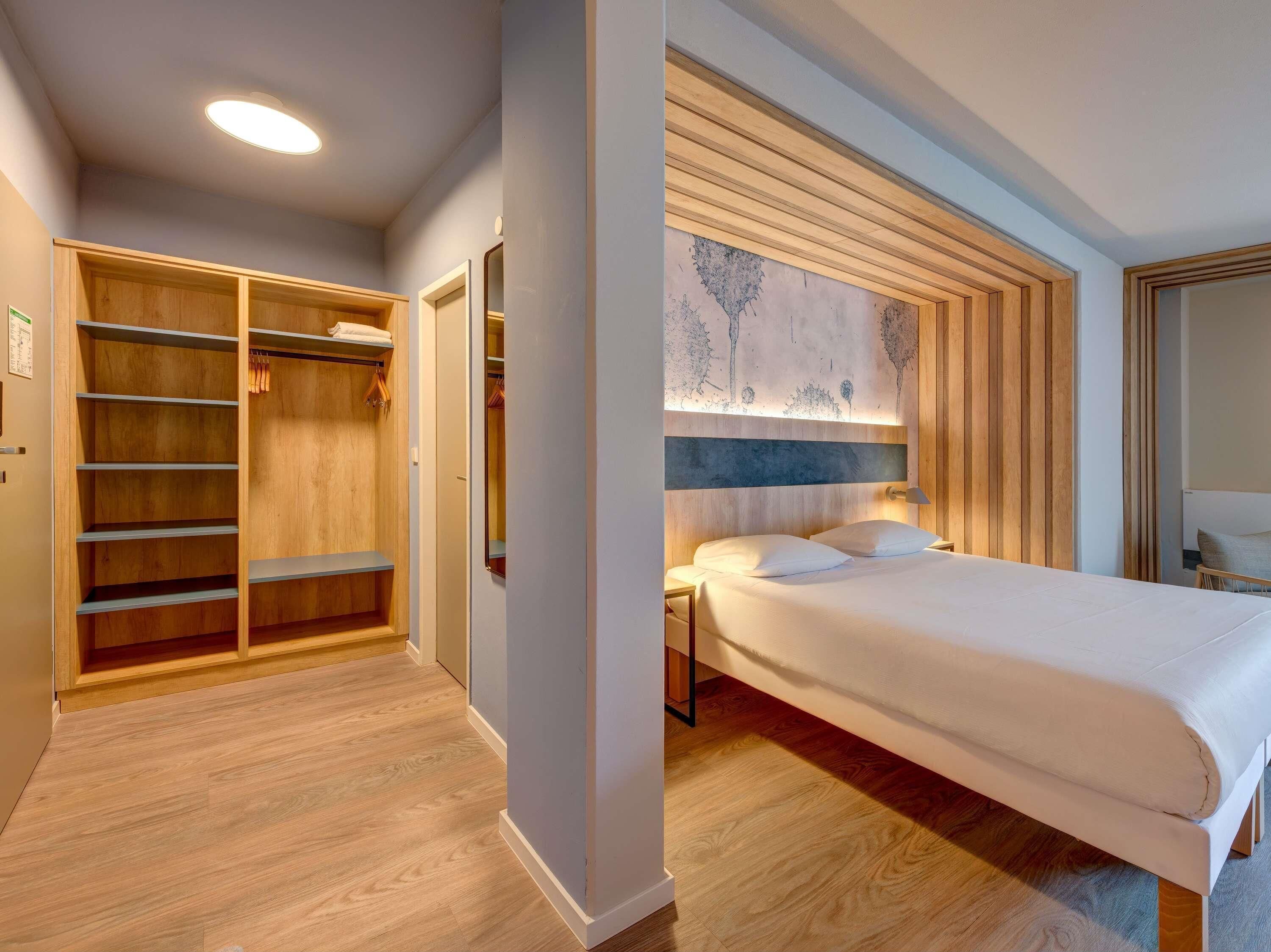 A hotel room with a bed, a wooden wardrobe, and a nightstand.