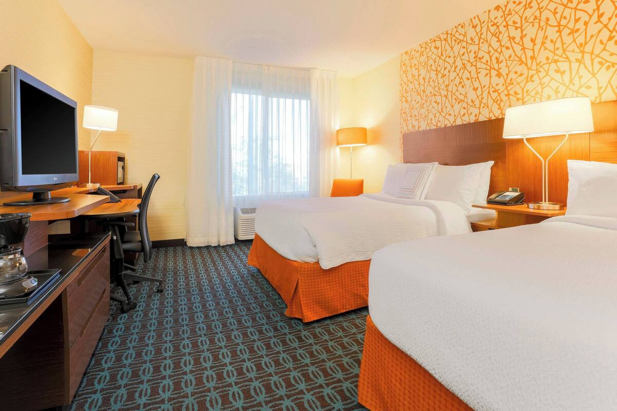 A hotel room with a bed, a desk with a computer, a TV, and a lamp.